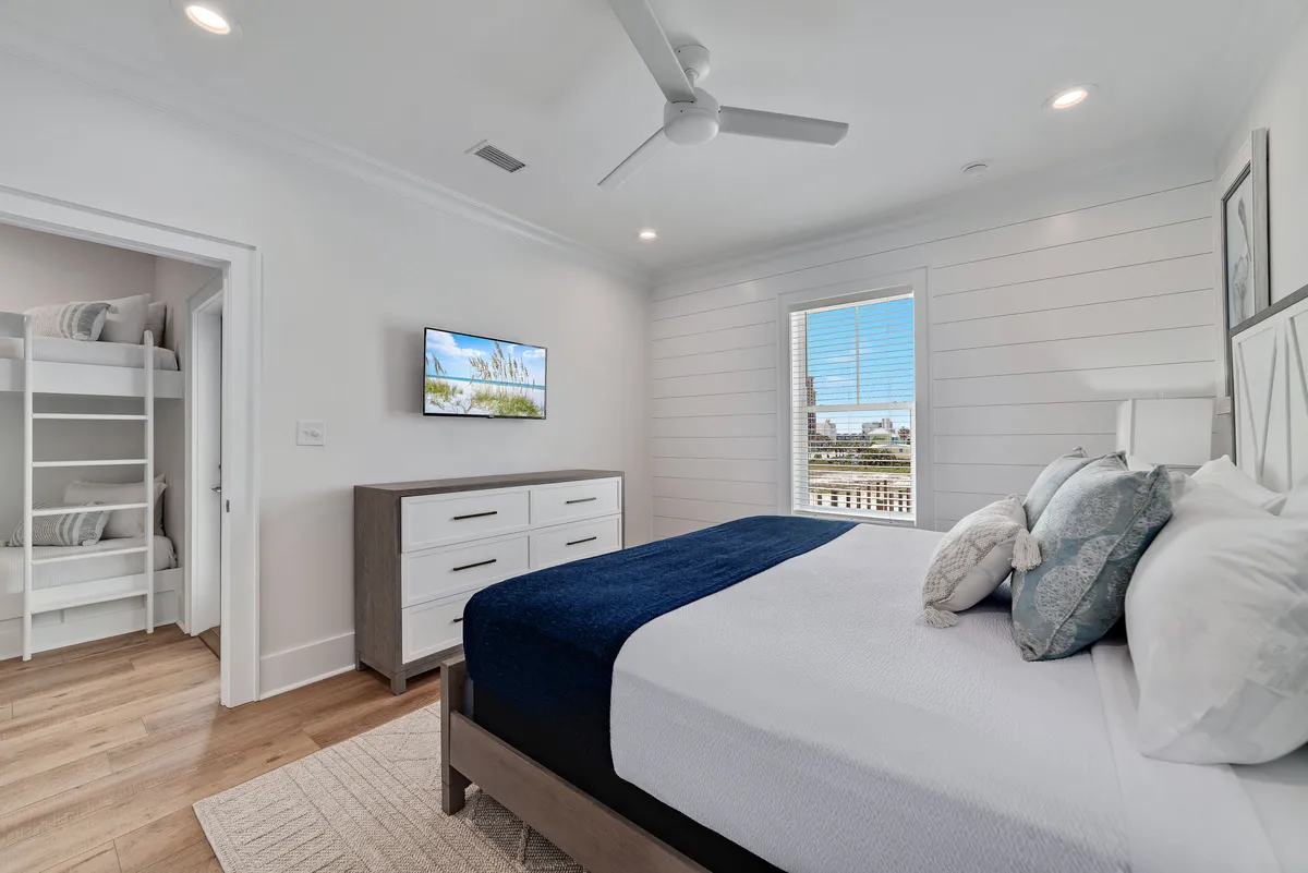 A multi-purpose bedroom with a bed featuring blue accents, a set of bunk beds, a dresser, a television, and a window with a pleasant view. The space radiates comfort and is ideal for families spending time together.