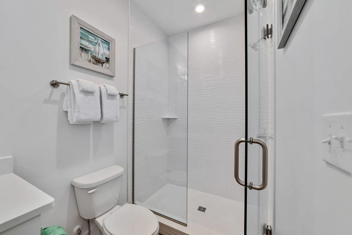 A sparkling modern bathroom featuring a glass shower enclosure, fluffy white towels, and a spotless toilet. The clean lines, uncluttered surfaces, and fresh towels emphasize meticulous attention to hygiene and comfort.