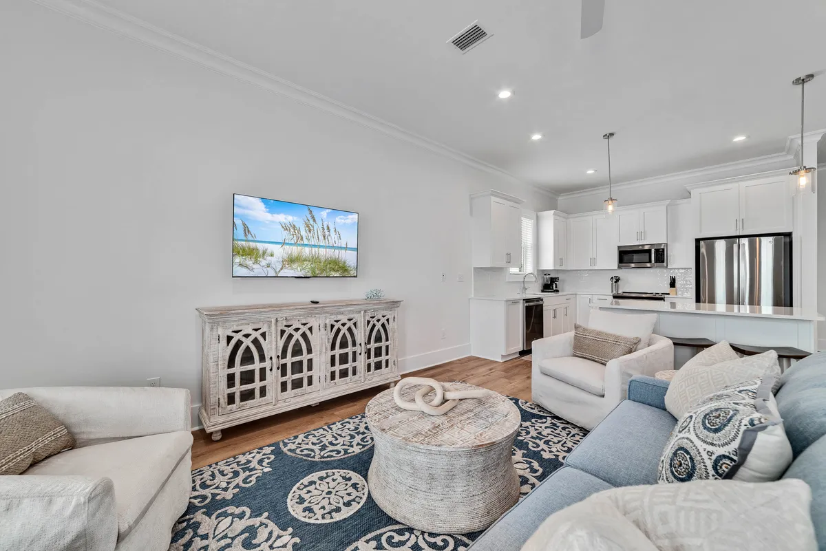 A welcoming living area featuring a comfortable sofa with plush cushions, a circular coffee table, and a decorative cabinet. The television displays a calming beach scene, and the space is arranged for group relaxation and entertainment.