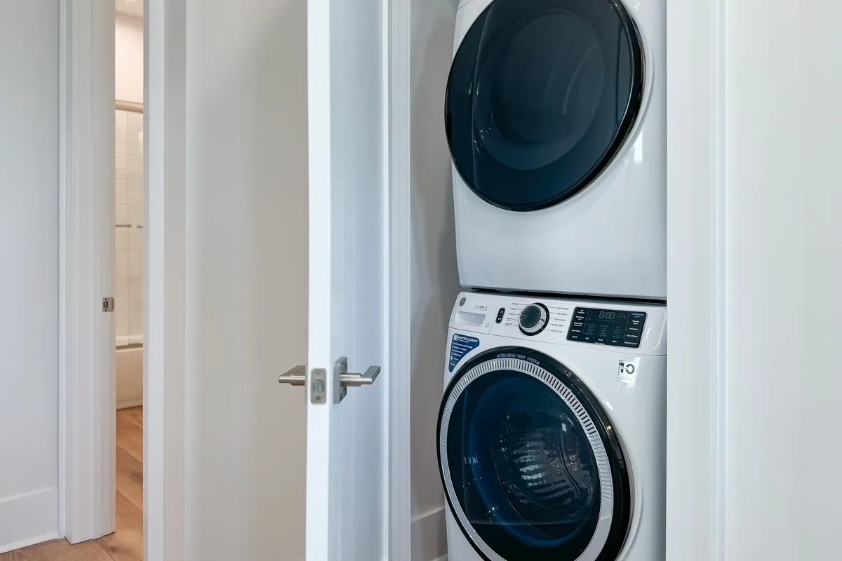 A practical laundry nook with a stacked washer and dryer, situated by a doorway to a clean bathroom. The area is uncluttered and reflects the home's ongoing commitment to freshness and hygiene for guests.