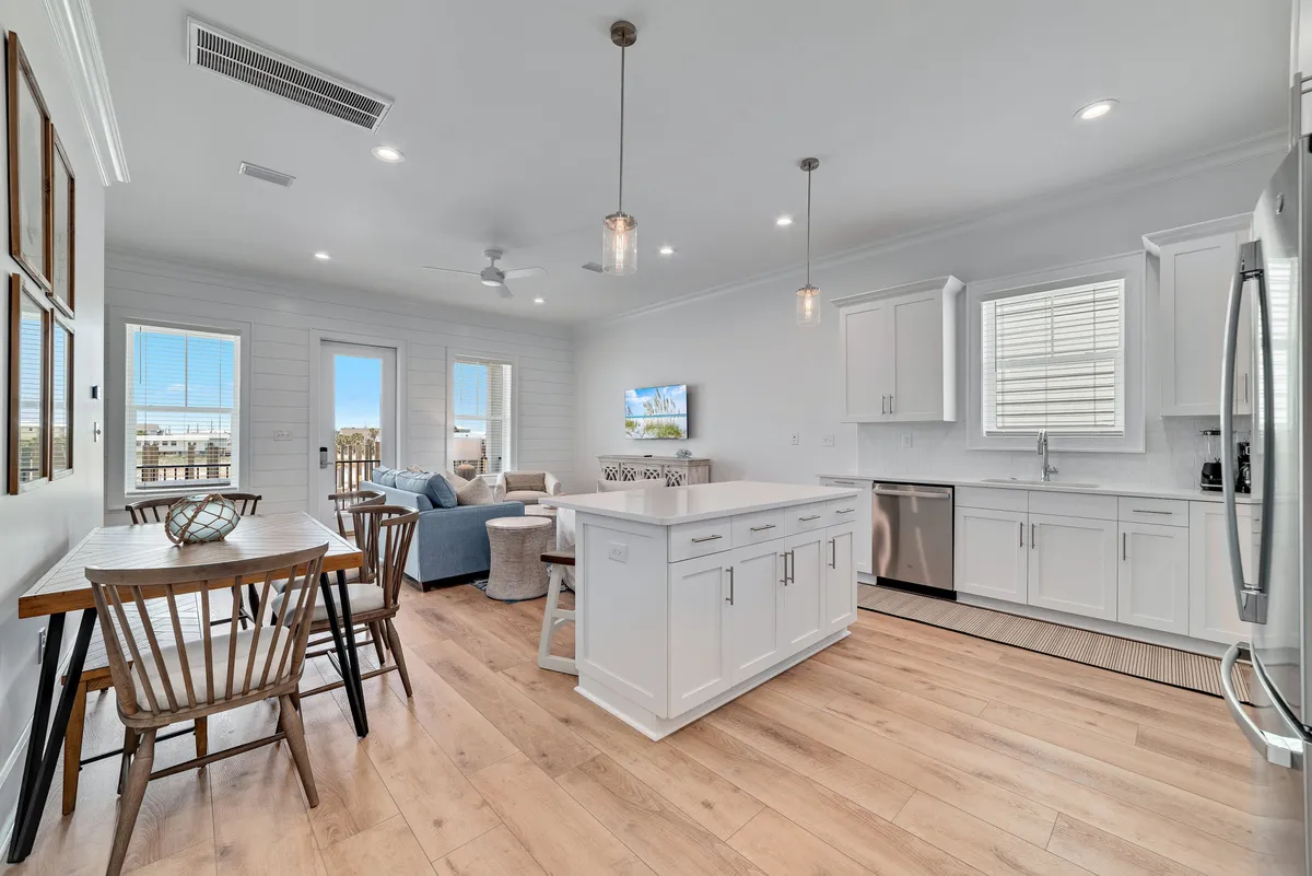 An open-plan living space with a large wall-mounted TV, kitchen island with seating, dining table, and a comfortable couch and ottoman. The space is designed for socializing and family gatherings, with ample light and a welcoming ambiance that encourages relaxation and togetherness before or after exploring the area.