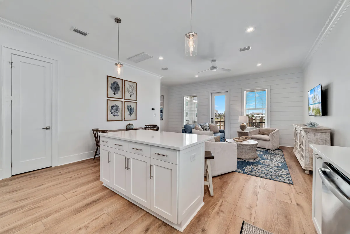 A spacious, light-filled open-plan area combines a modern kitchen island with inviting living and sitting spaces. The island features storage and pendant lighting, while a comfortable sofa and armchair face a wall-mounted Smart TV. Coastal-themed wall art and warm wooden flooring create a relaxed, stylish ambiance, perfect for socializing and unwinding after a day’s adventures.