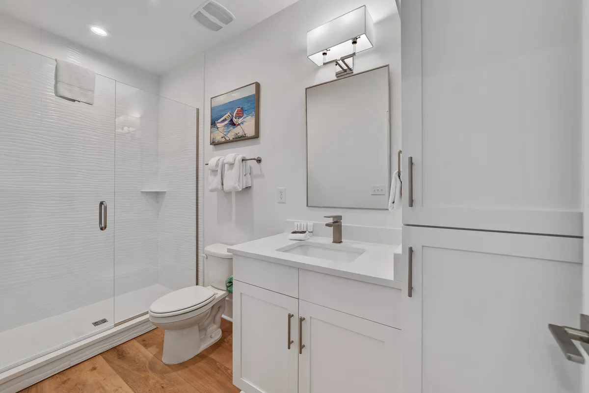 A sparkling en-suite bathroom with a glass-enclosed shower, white vanity, modern fixtures, and beach-themed decor. Fresh towels are neatly folded, and the space is bright and pristine.